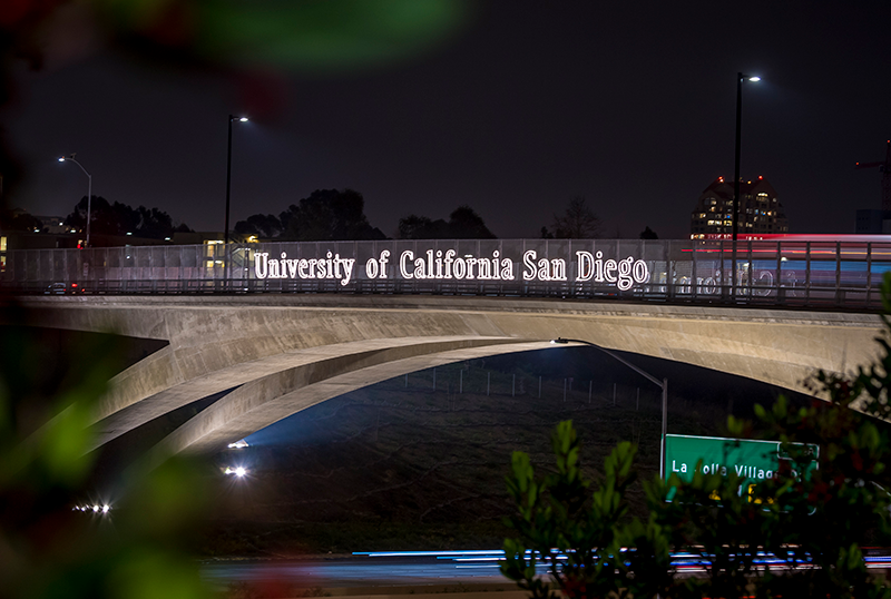 Gilman Bridge illuminated at night. The sign on the bridge reads "UC San Diego"